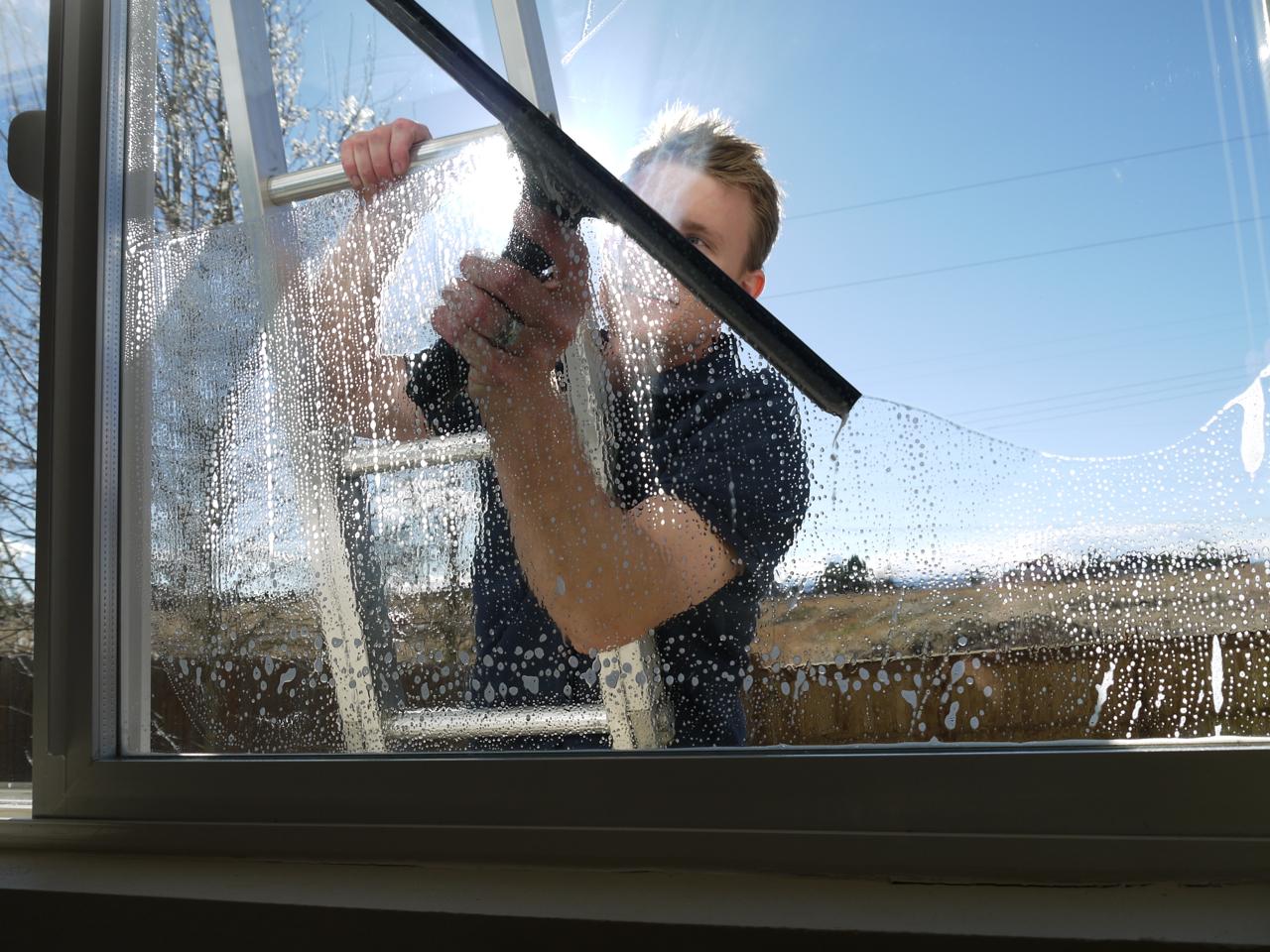 a man on ladder cleaning windows from outside and the picture take from inside.